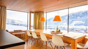 Un espace de restauration moderne avec une table en bois, des chaises blanches et de grandes fenêtres donnant sur un paysage enneigé.