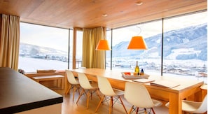 Un comedor moderno con una mesa de madera, sillas blancas y ventanas amplias con vistas a una montaña nevada.