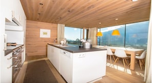Cocina moderna con isla central, comedor con mesa y sillas, y ventanas amplias con vistas al exterior.