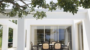 An outdoor patio with a table and chairs, large glass doors, and a white building structure. - Eliofos Luxury Villa - Private Pool, Wifi, BBQ, Smart TV  (Neo Chorio)