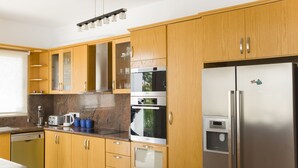 A modern kitchen with wooden cabinets, stainless steel appliances, and a built-in oven. - Eliofos Luxury Villa - Private Pool, Wifi, BBQ, Smart TV  (Neo Chorio)
