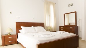 A neatly made bed with white linens, a wooden headboard, a bedside table with a lamp, and a mirror on the wall. - Eliofos Luxury Villa - Private Pool, Wifi, BBQ, Smart TV  (Neo Chorio)