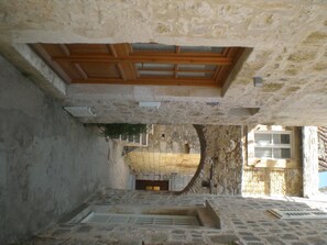 Une ruelle étroite pavée de pierres, avec une porte en bois sur la gauche et une arche en pierre au centre.