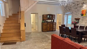 Una escalera de madera que lleva a un baño, un comedor con una mesa y sillas, y un piso de piedra.