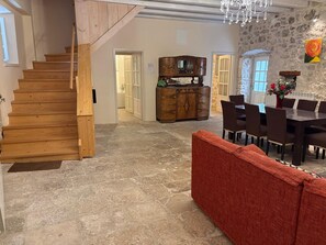 A wooden staircase leading to a bathroom, a dining area with a table and chairs, and a stone floor.