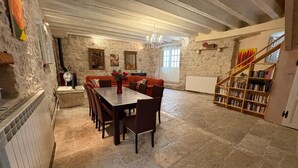 Un comedor con suelo de piedra, una mesa y sillas de madera, un sofá rojo y una estantería.