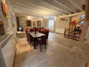 A stone-floored dining area with a wooden table and chairs, a red sofa, and a bookshelf.