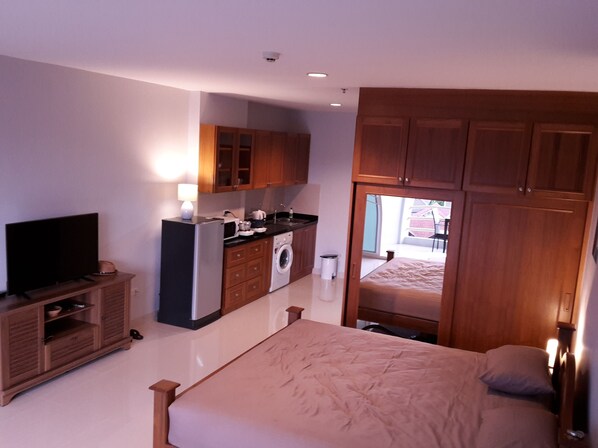A bedroom with a bed, a TV, a washing machine, and a kitchenette. - View Talay 5D Jomtien Beach Pattaya R192 (Pattaya)