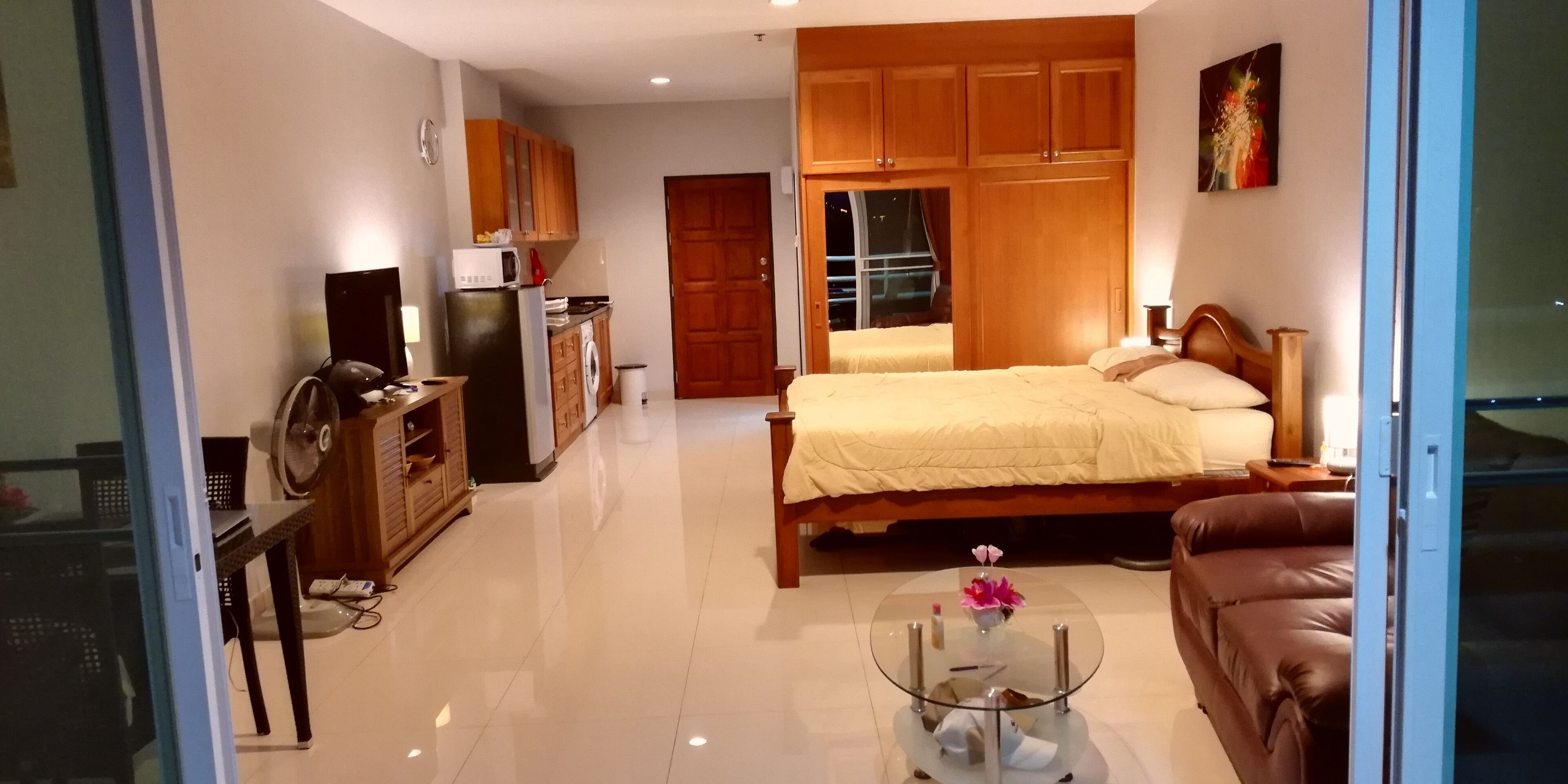 A compact hotel room with a bed, a sofa, a small table, a TV, a microwave, and a wardrobe.