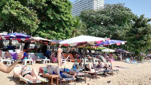 Ein Strand mit mehreren bunten Sonnenschirmen, Liegestühlen und entspannten Menschen.