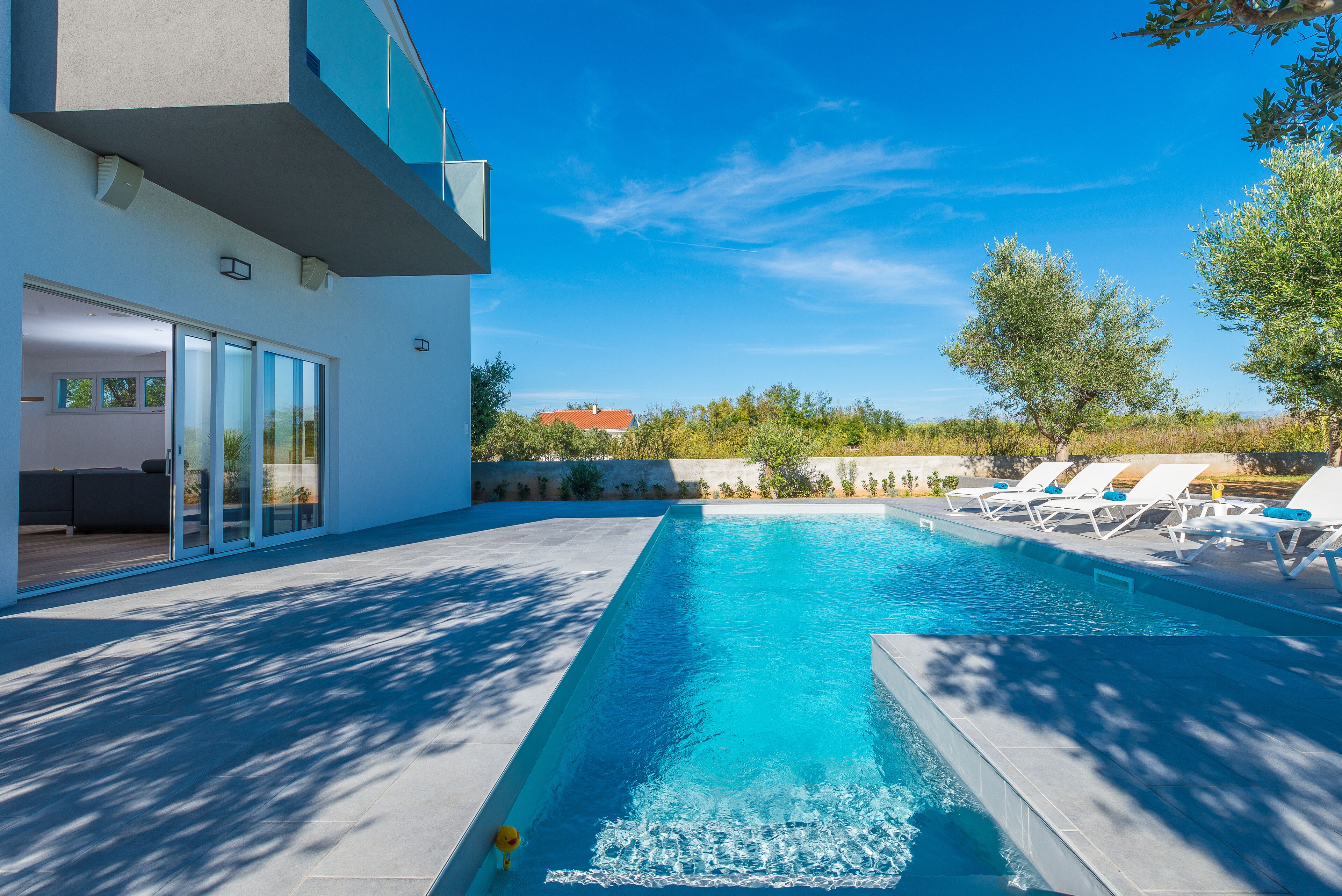 Un espace piscine moderne avec un ciel bleu dégagé, une piscine et des chaises longues.
