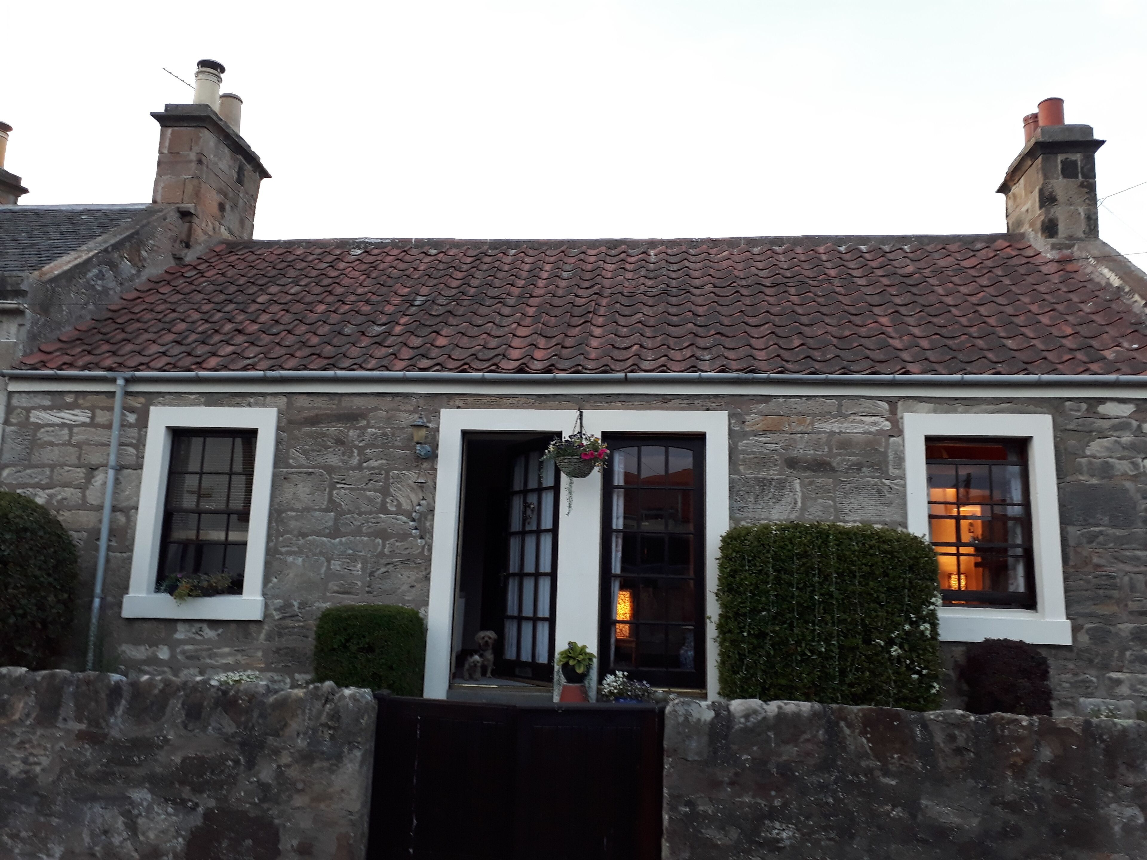Un edificio de piedra con techo de tejas y dos chimeneas, y un perro pequeño en el porche.