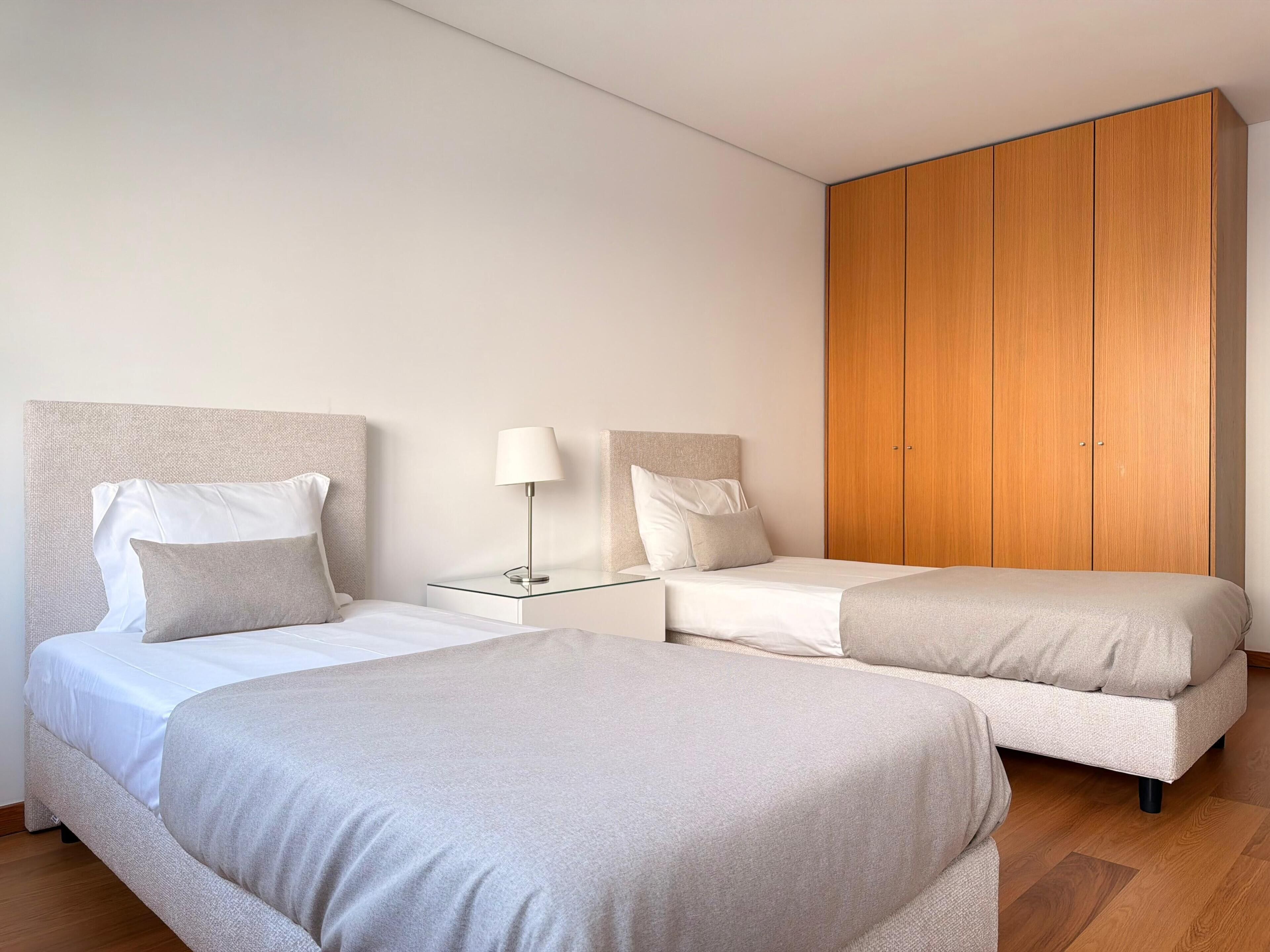 A hotel room with two beds, a nightstand with a lamp, and a wooden wardrobe.