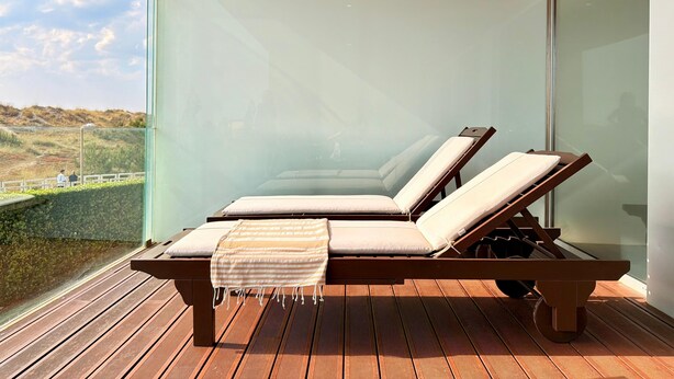 Een balkon met houten vloer en twee loungesteunen met kussens.