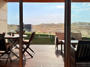 Une terrasse extérieure avec une table et des chaises, et une porte vitrée donnant sur un paysage vallonné.