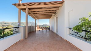 Un balcón con una pérgola, una mesa con sillas y vistas a montañas.