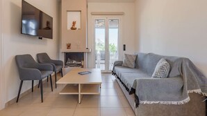 Una sala de estar moderna con una televisión de pantalla plana, dos sillones grises, una mesa de centro de madera, un sofá gris con una manta y una chimenea.