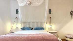 A bedroom with a bed, white curtains, two bedside lamps, and a decorative wall piece.