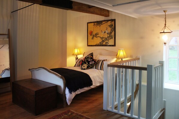 A bedroom with a bed, bedside lamps, a wooden chest, a painting, and a window.