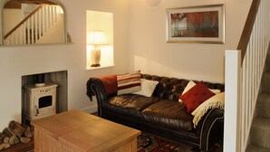 A cozy living room with a leather sofa, a wooden coffee table, a fireplace, a mirror, a lamp, and a framed picture on the wall. - Romantic & Secluded Cottage. Beautiful Walks & Fantastic Pub (Ashbury)
