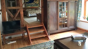 Ein Zimmer mit freiliegenden Holzbalken, einem Bett mit floralem Überwurf, einem Holzkabinett mit Glastüren und einem kleinen Tisch mit einer Dekoration.