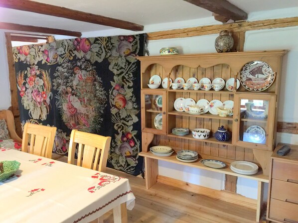 A dining area with a wooden table and chairs, a floral tapestry, and a display of various dishes and pottery on shelves. - Secluded apartment above the stables in a historical mill house (Platerowka)