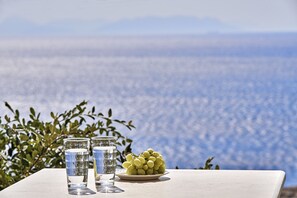 Une table avec deux verres d’eau et une assiette de raisins, le tout placé devant un paysage marin pittoresque.