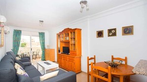 Una sala de estar con sofá, una mesa de comedor con sillas, un televisor y un mueble de madera.