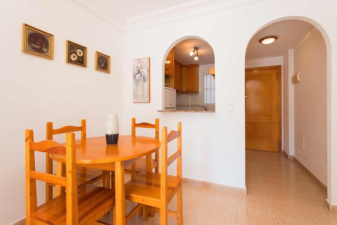 A dining area with a round wooden table and chairs, a vase, and framed artwork on the wall.