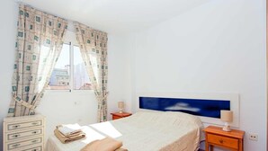 Un dormitorio con cama, cómoda, mesita de noche y ventana con cortinas.