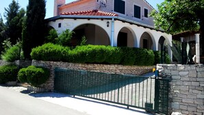 Eine Villa mit einer Steinmauer, einem grünen Tor und Rundbogenfenstern.