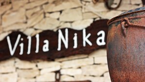 Ein rustikales Schild mit der Aufschrift "Villa Nika" an einer Steinmauer, im Vordergrund ein großer, verrosteter Metalltopf.