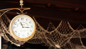 Eine Grand Central Terminal Uhr mit rustikalem Design, die über einem verzierten Netz hängt.