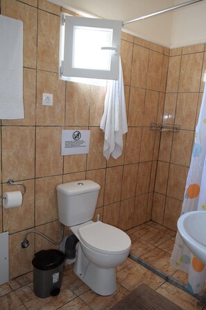 A bathroom with a toilet, a trash bin, a towel rack, and a shower curtain.