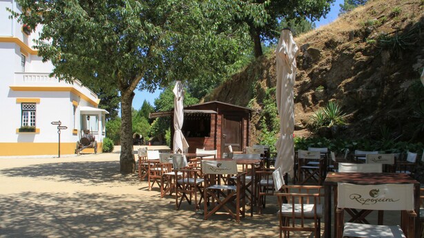 Un espace extérieur aménagé pour les repas, avec des tables et des chaises en bois, une petite structure en bois et un bâtiment blanc en arrière-plan.