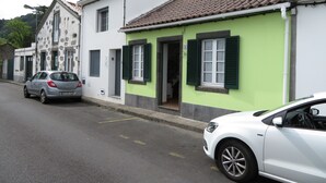 A street with buildings, one with green shutters and a white facade, and parked cars. - Casa Formosa das Furnas (Povoação)