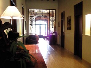 A hallway with a wooden floor, a lamp, a plant, and a door with a decorative metal gate. - Valencia Country Hotel - Villamilagro (Polinyà de Xúquer)