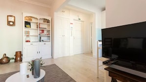 Una sala de estar con una televisión de pantalla plana, una estantería, una mesa de centro y una puerta que da a otra habitación.
