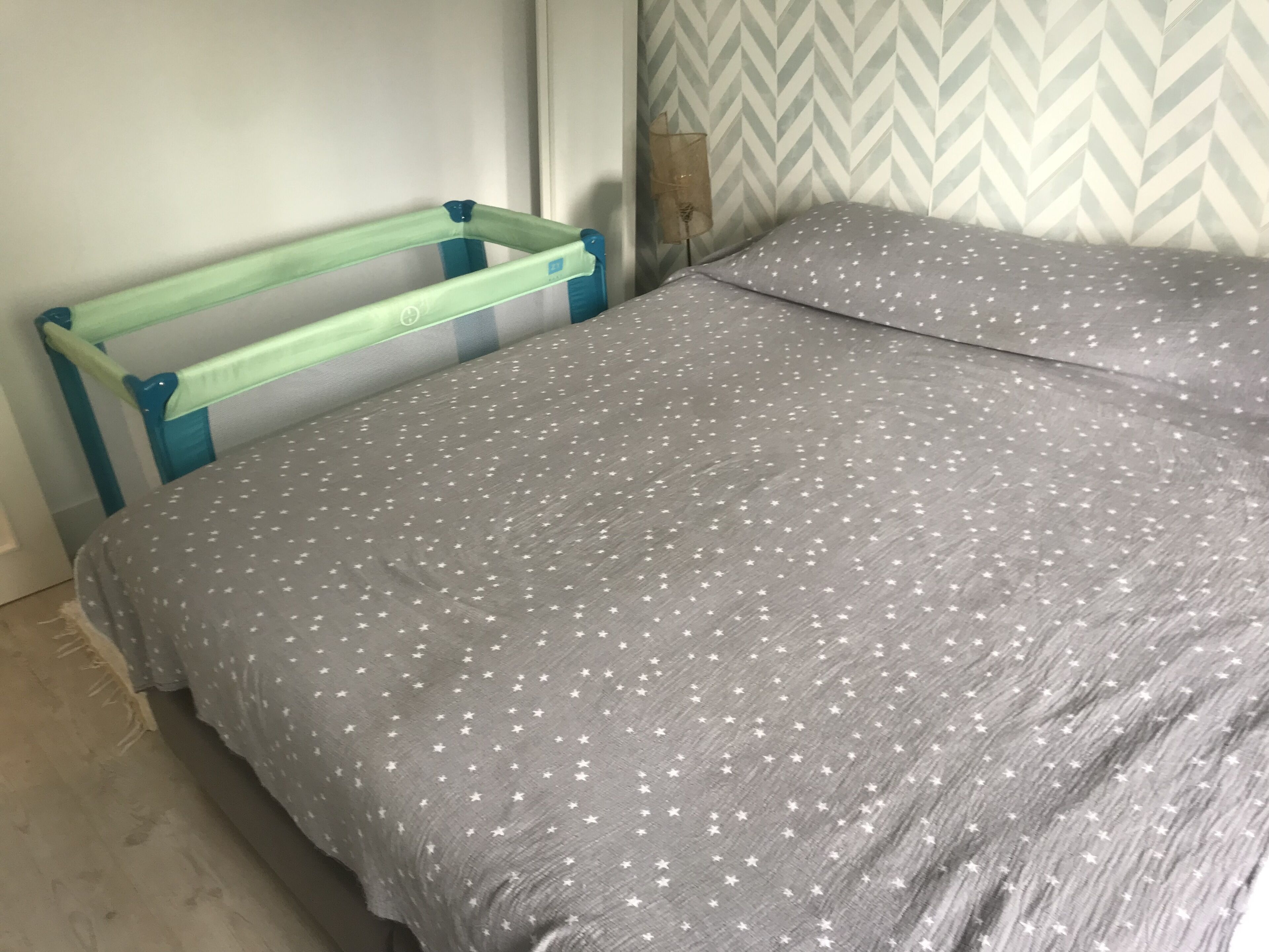 A bed with a grey bedspread featuring white stars, a blue headboard, and a wall with a chevron pattern.