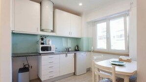 Una cocina compacta con armarios blancos, microondas, refrigerador pequeño y ventana que proporciona luz natural.