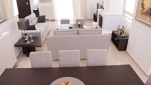 A modern living room with a sofa, two side tables, a coffee table, and a dining table with a fruit bowl.