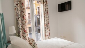 Un dormitorio con cama, televisión y ventana con cortinas.