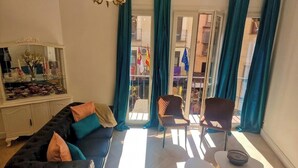 Una sala de estar con sofá, sillas, una mesa, una araña y vistas a través de un ventanal.