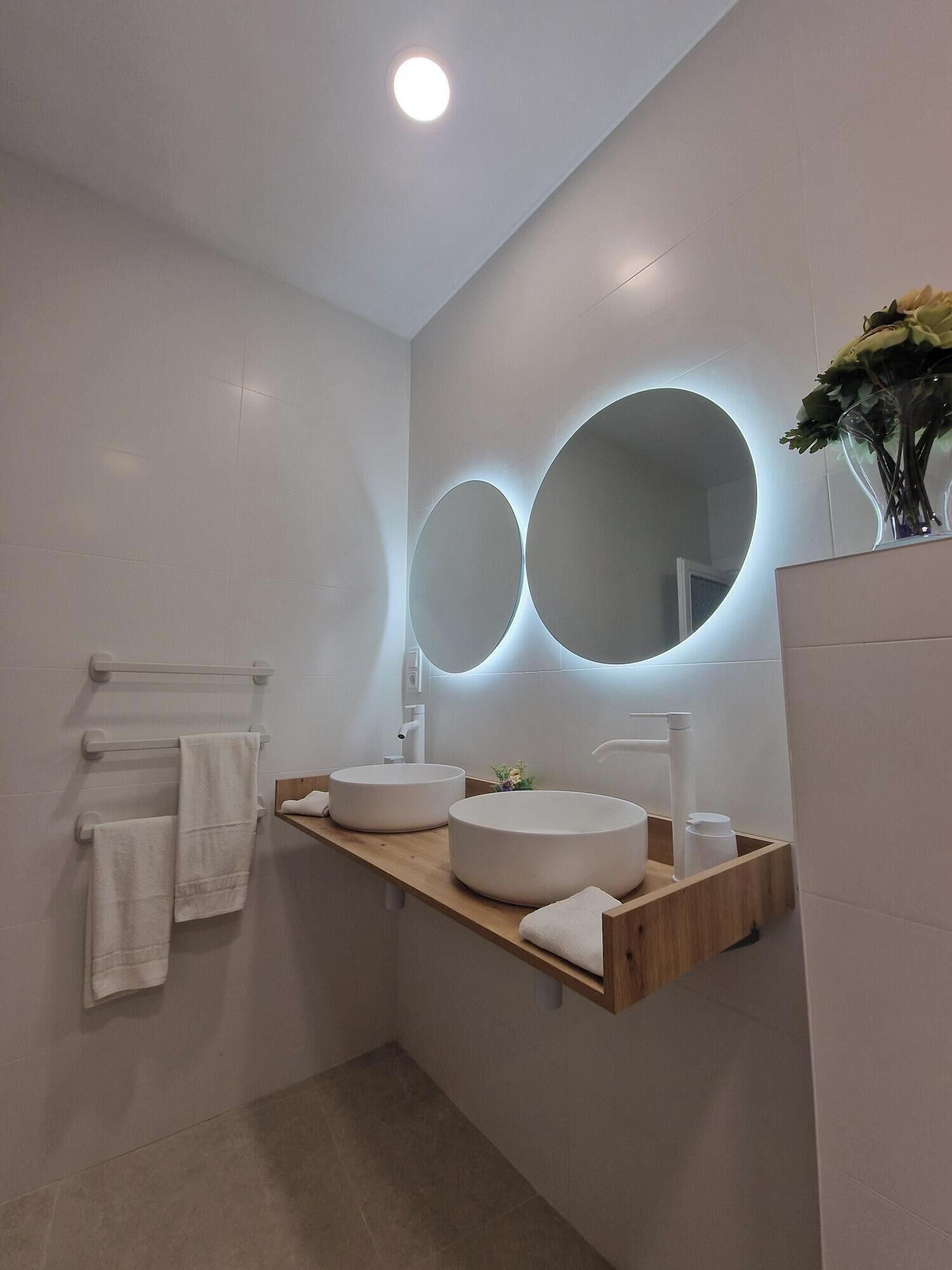 Un bagno moderno con due specchi circolari, un mobile contenitore in legno e un lavandino bianco.