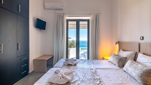 Une chambre d’hôtel équipée d’un lit, d’une télévision, d’un bureau et offrant une vue sur la mer grâce à une porte vitrée.