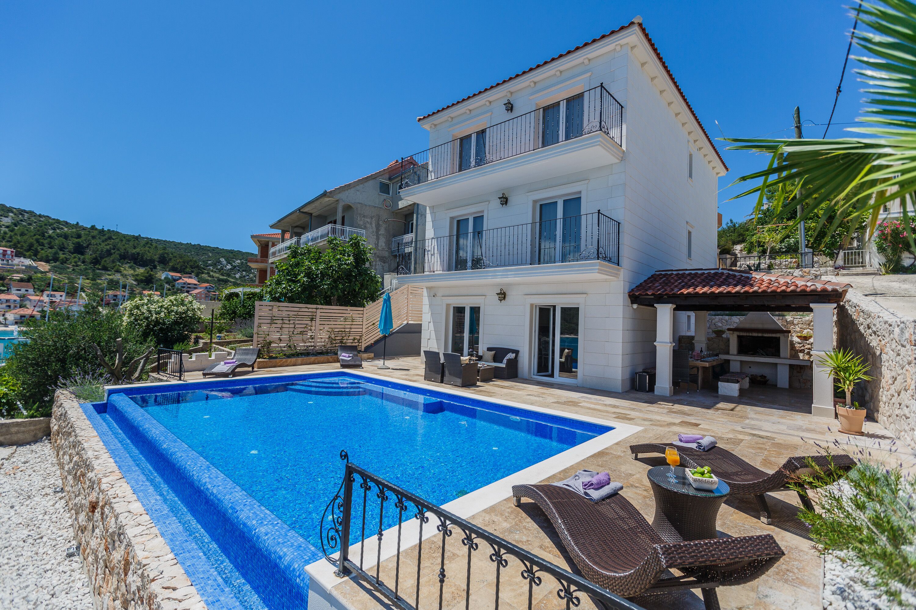 Una casa de dos pisos con piscina, mobiliario exterior y zona de barbacoa.