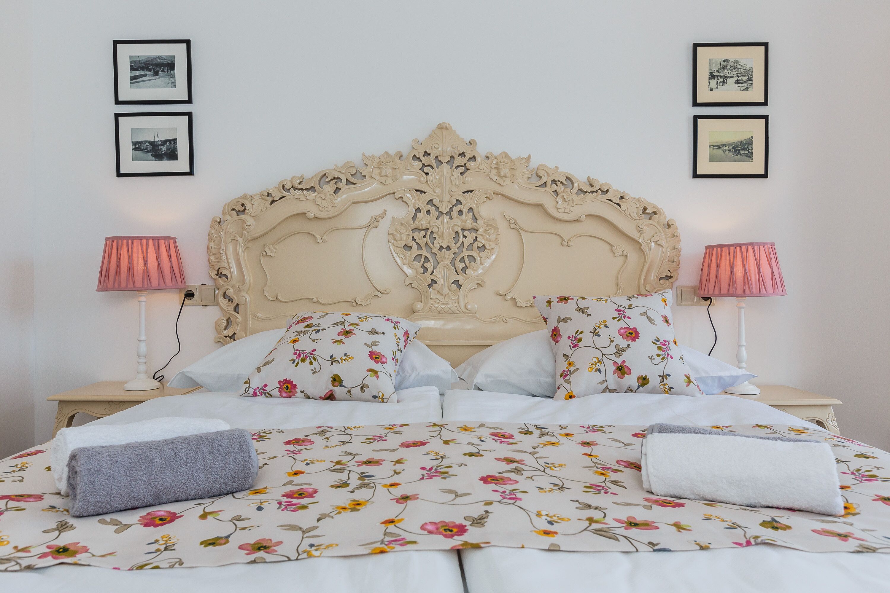 Ein ordentlich gemachtes Bett mit floralem Bettbezug, einem dekorativen Kopfteil und zwei Nachttischlampen.