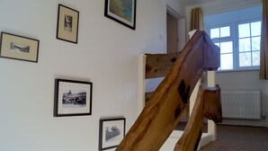 A staircase with a wooden handrail and a view of a room with framed pictures on the wall and a window with curtains. - 'The Stables'. A lovely stone built cottage in the small village of Powburn. (Powburn)