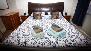 Cama bem arrumada com colcha estampada, dois travesseiros e toalhas dobradas ao lado.