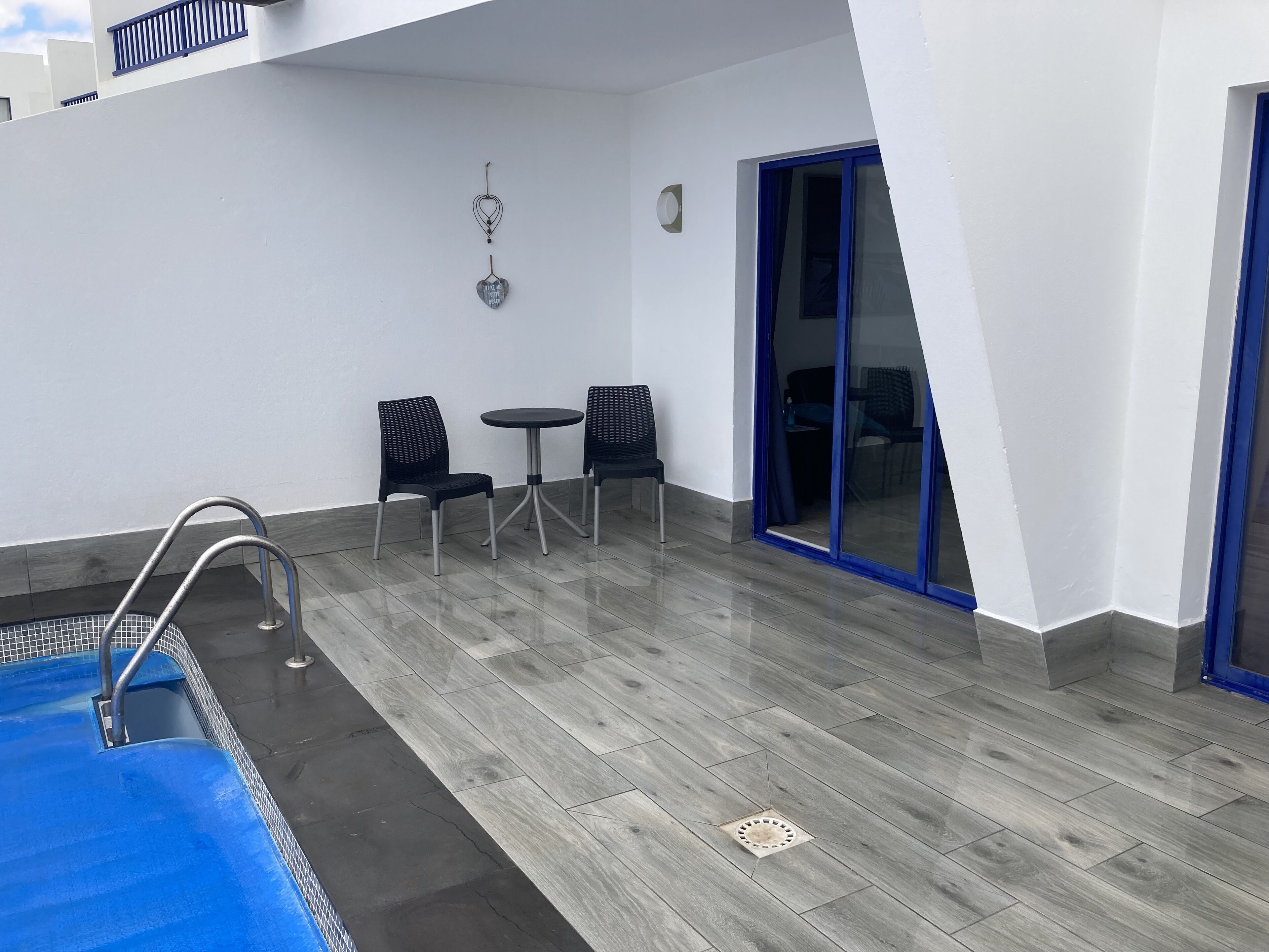 A pool area with a blue pool, two black chairs, a small round table, and a blue-framed sliding door.
